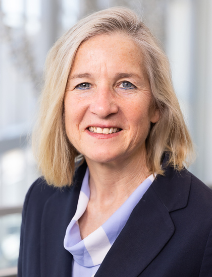 woman with shoulder-length light blonde hair, cowl neck blue and white checkered blouse, navy blazer