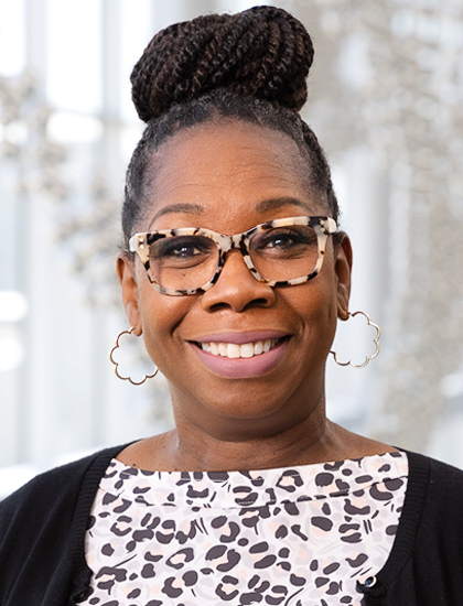 woman with tortoise shell glasses and braids in a top bun, black sweater, black, pink, white shapes on blouse