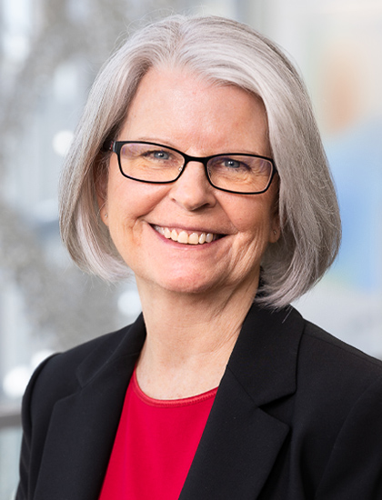 woman with bobbed frosted hair and glasses, black jacket, red shirt