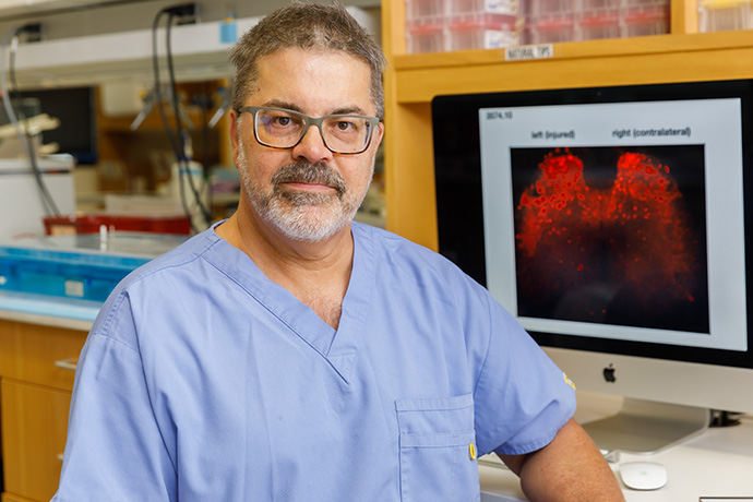 Dr. Henkemeyer, with gray hair and trim beard wearing scrubs, standing in a lab.