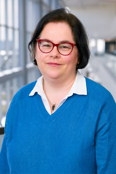 woman in white shirt and blue sweater, red glasses, short dark hair