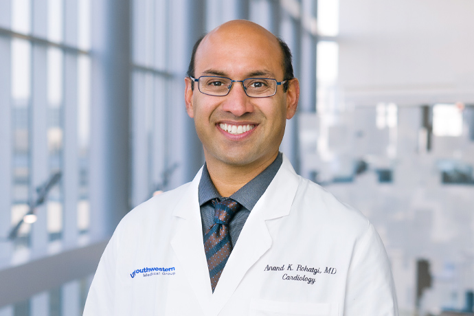 headshot of smiling doctor with balding dark hair and glasses wearing white medical coat over grey shirt and tie