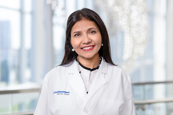Smiling woman with long dark hair wearing pearl earrings and a UT Southwestern lab coat.