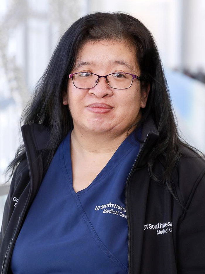 woman in black jacket, blue scrubs, long dark hair with glasses