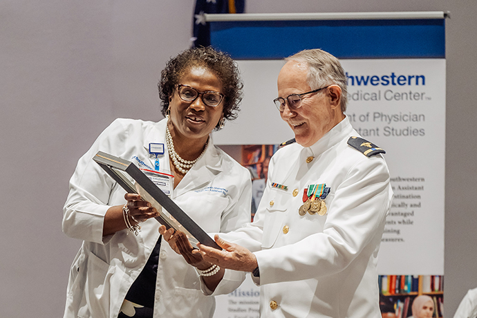 Dr. Howell-Stampley, wearing a lab coat, receiving her plaque from Dr. Jones, wearing a white uniform.