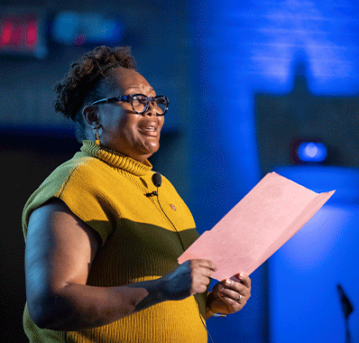 woman in yellow sweater recites poetry from book