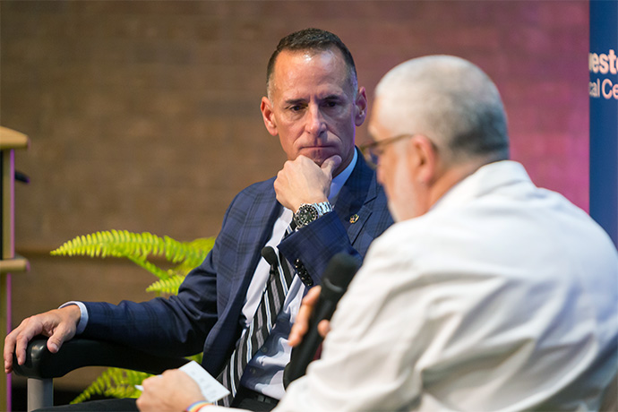 In a fireside chat, Mr. Poole (left) in blue and gray plaid shirt, talks with, hared with Timothy Blackburn, Ph.D., Professor of Radiology, gray-haired man in white shirt.