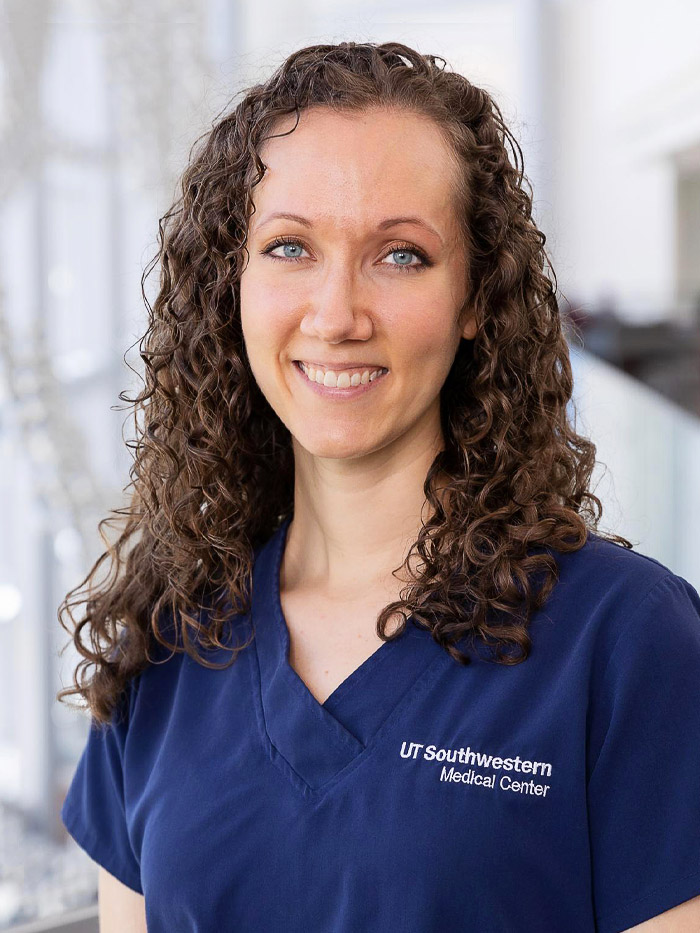 woman with brown shoulder length curly hair, wearing blue scrubs