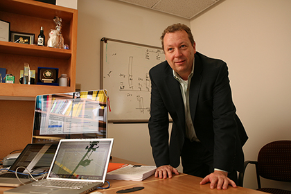 Man wearing a business suit, in an office, leaning on a desk.