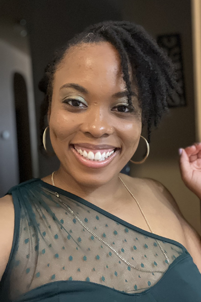 Smiling woman with dark curly hair, wearing a black dress.