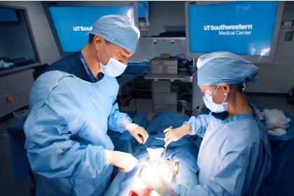 man and woman in blue surgical scrubs work on simulated patient on operating table