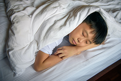 Teen with dark hair sleeping in bed.