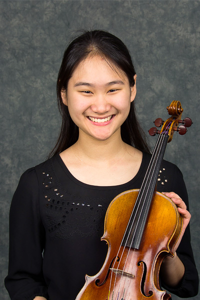 Smiling young woman with long dark hair wearing a black shirt and holding her violin.
