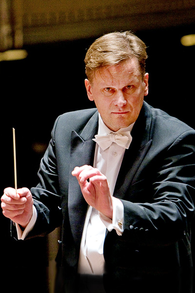 Intense man with neat brown hair wearing a tuxedo and waiving his arms.