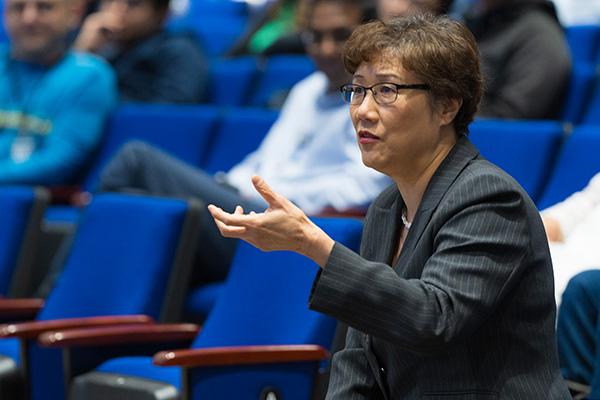 A woman with dark hair and glasses asking a question from the audience.