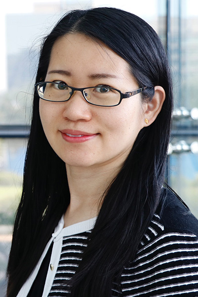 Smiling woman with long dark hair and glasses, standing in front of window with view of downtown Dallas.