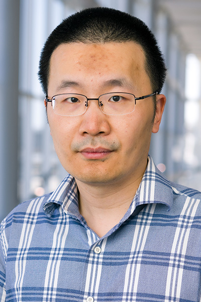 Man with short dark hair, wearing glasses and a plaid shirt.