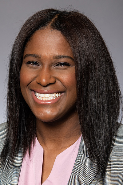 Smiling woman with long dark hair, wearing a pink blouse and gray jacket.