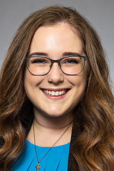 Smiling woman with long brown hair, wearing a blue blouse and glasses.