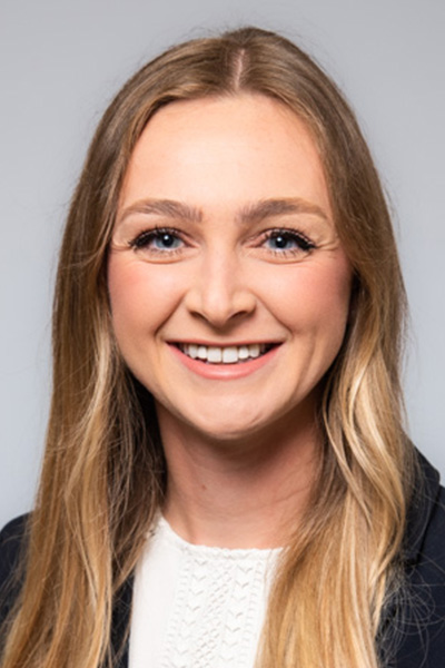 Smiling woman with long blond hair, wearing a white blouse and dark jacket.