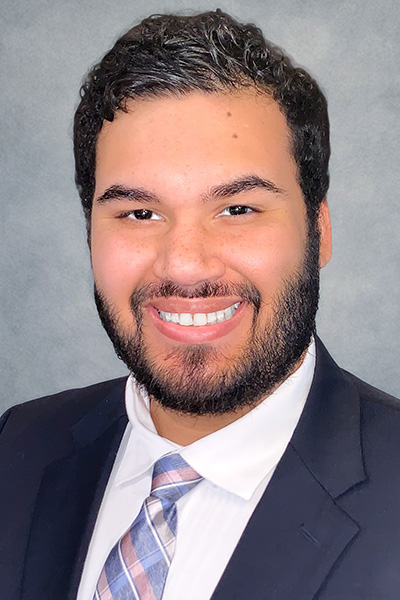 Smiling man with dark hair, trim beard, and mustache, wearing a dark suit and tie.