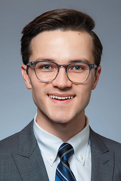 Smiling man with short dark hair, wearing a gray suit, striped tie, and glasses.