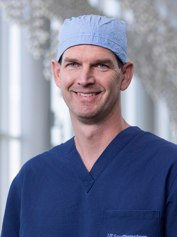 Smiling man wearing blue UT&nbsp;Southwestern scrubs and blue surgical cap.