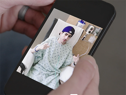 Man wearing a hospital gown, oxygen tube, and baseball cap in an infusion chair.