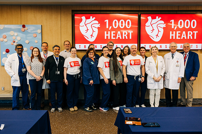 17 men and women posing in front of 1,000 Heart Transplant banners.
