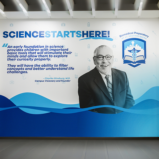 blue and white mural Science Starts Here with image of smiling older man in suit wearing round glasses and logo of Biomedical Preparatory