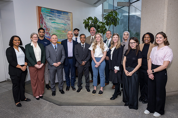 after the 2026 Capra Symposium, a group of 15 UTSW medical students, guests, and faculty stand in front of glass wall and painting