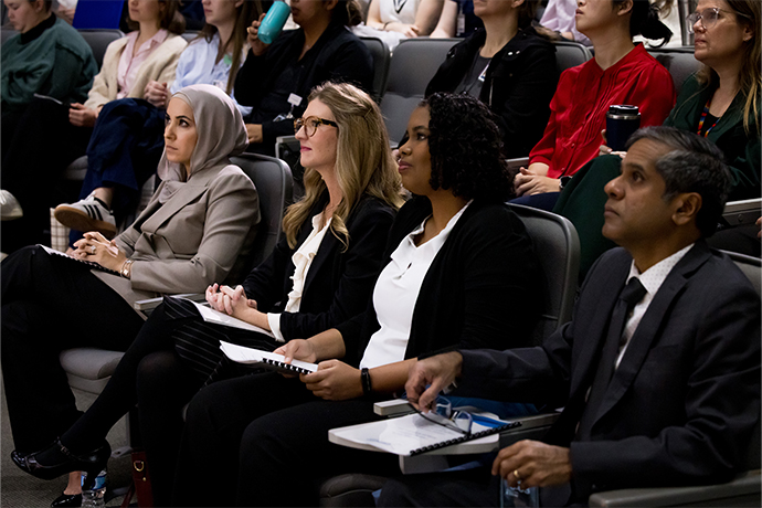 4 Capra Symposium leaders sit at front of auditorium during presentations: from left - Dr. Asisad, Traci Betts, DPT, Yosanly Comelio, MD, MSc, and Dr. Sankaranarayanan