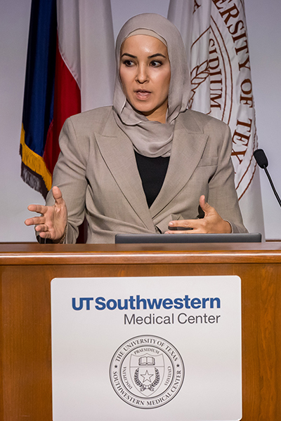 Omaira Azizad, M.D., wearing tan scarf and jacket speaks from podium