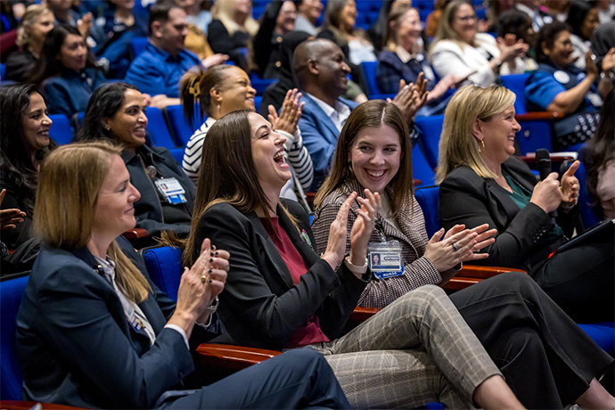 4 smiling women in foreground of audience clapping