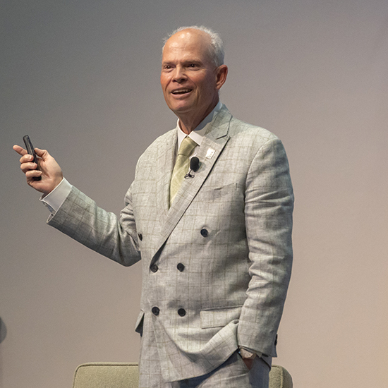 balding man in tan suit speaks on stage
