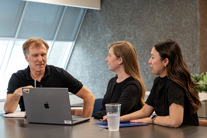 A man and two women sit at a table with a laptop computer.