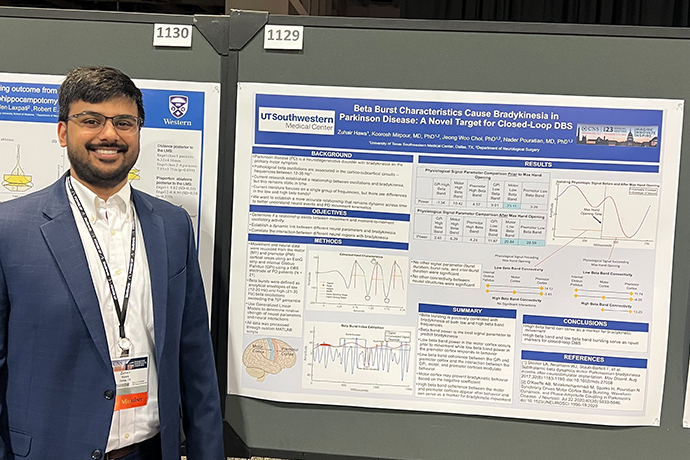 smiling man with glasses, dark hair and beard stands in front of research poster