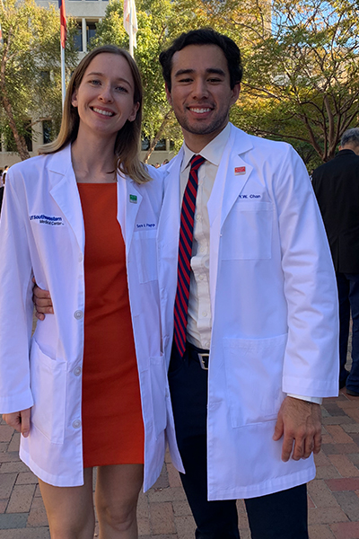 young woman and man outdoors wearing white lab coats stand side by side