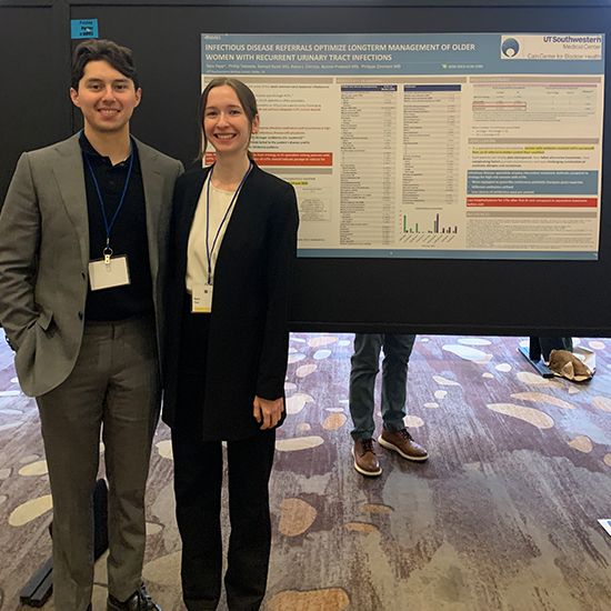 young man and woman stand proudly in front of research posters on wall