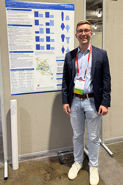young man in blue blazer with blond hair and glasses stands in front of research poster display