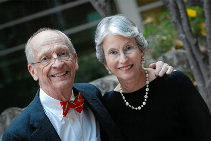 balding man with glasses and bow tie smiles and puts arm around woman with silver hair