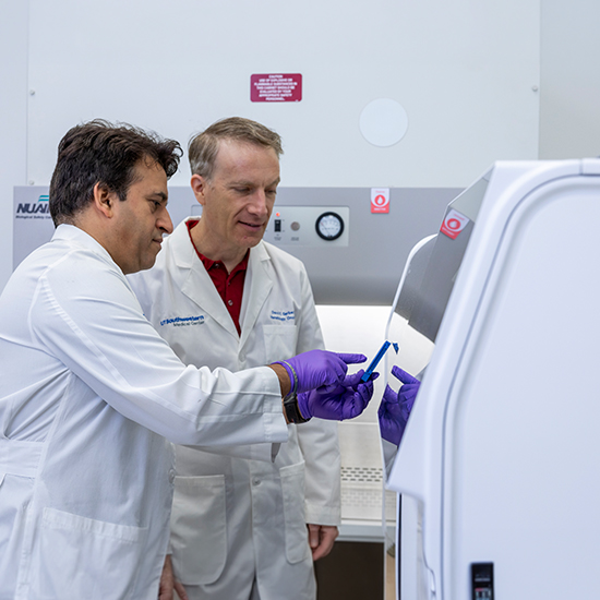 Scientist points out something on a large machine to a collegue.