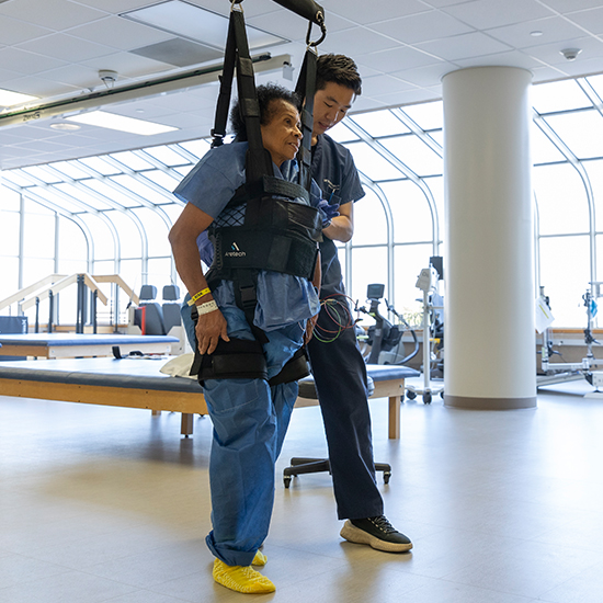patient walks using a robotic support system and their physical therapist in rehab facility