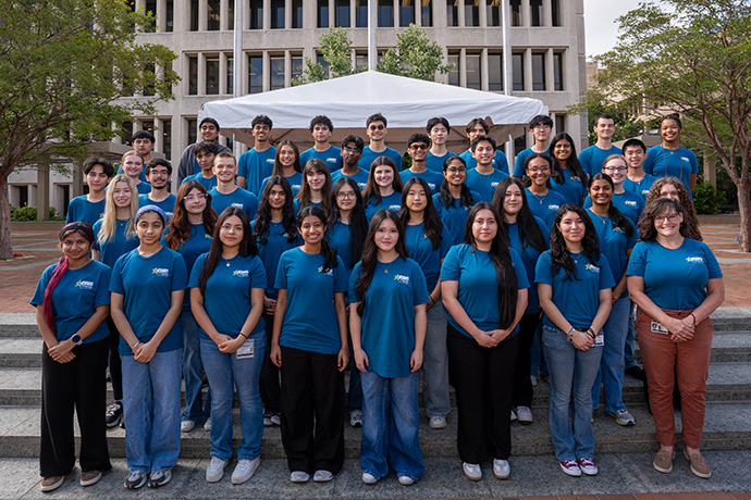 A large group of students wearing blue t-shirts posed on steps.