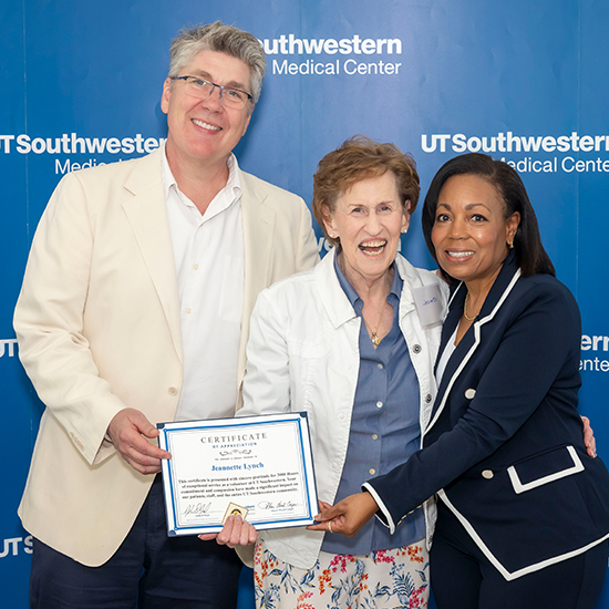 A smiling man and woman stand with a laughing woman holding up a certificate.