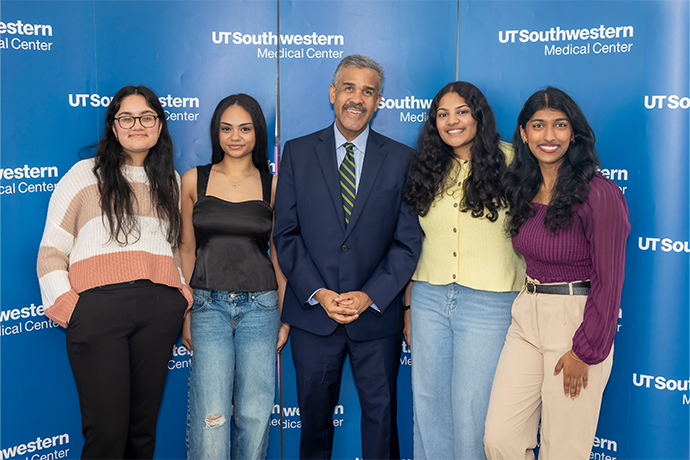 A man and four women smile as they pose together.