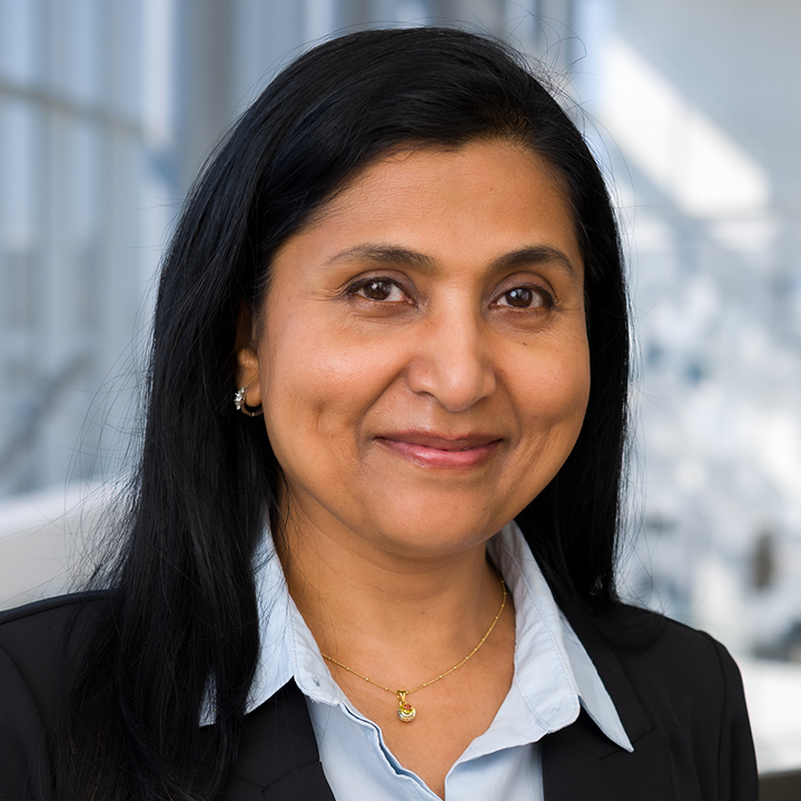 Shaila Cherian, smiling woman with dark hair against a glass window background