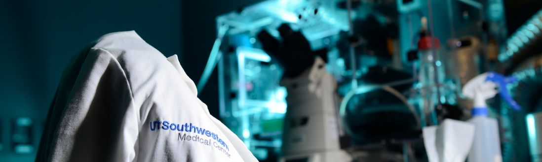 White lab coat with medical school logo on chair, microscope on lab table in background.