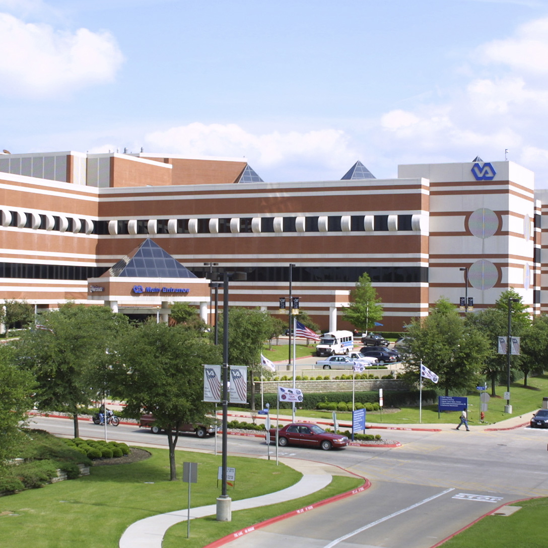 Tree lined roadway in the foreground with brown and while building in the background