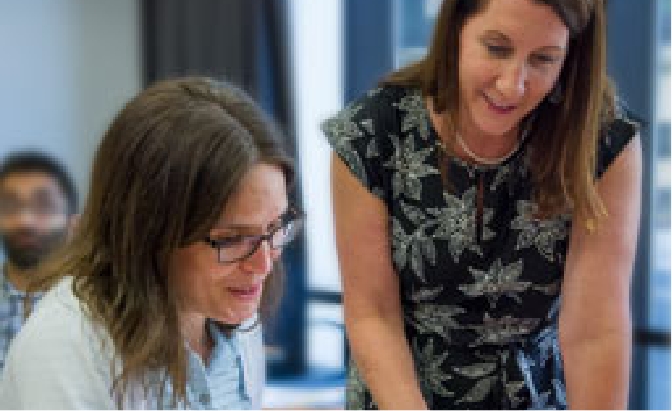 Two women, one with glasses, looking down while talking